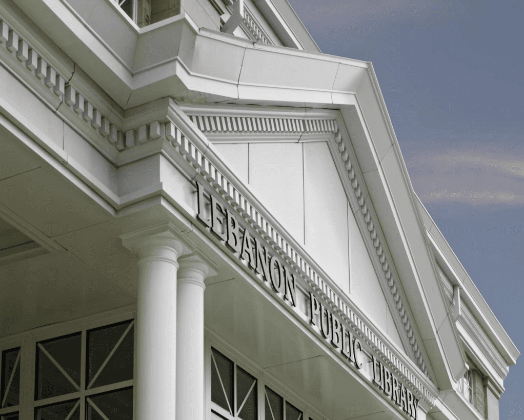 Exterior of the Lebanon Public Library building featuring classical architectural elements, including columns and detailed moldings, with a clear, blue sky background.